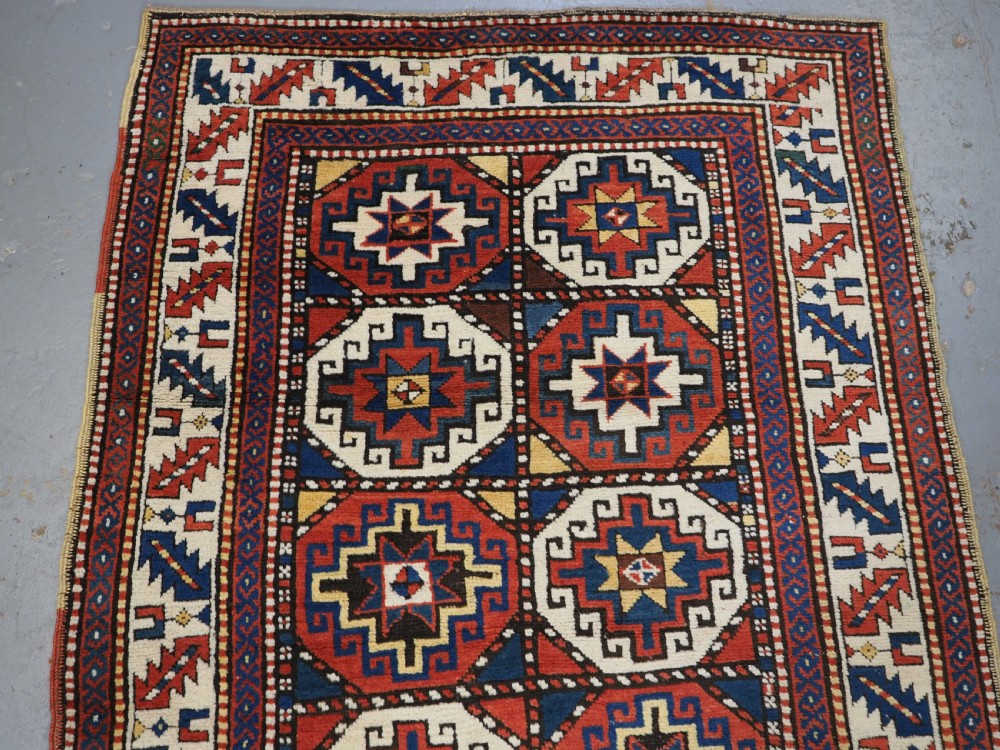 An antique Caucasian Moghan Kazak long wool rug featuring two vertical columns of octagonal geometric medallions in red, navy blue, cream, yellow, and green within a decorative patterned border. View III