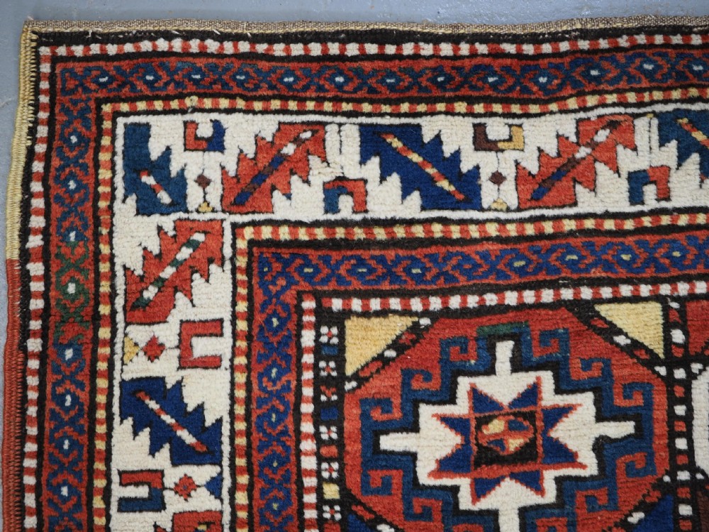 An antique Caucasian Moghan Kazak long wool rug featuring two vertical columns of octagonal geometric medallions in red, navy blue, cream, yellow, and green within a decorative patterned border. View VI