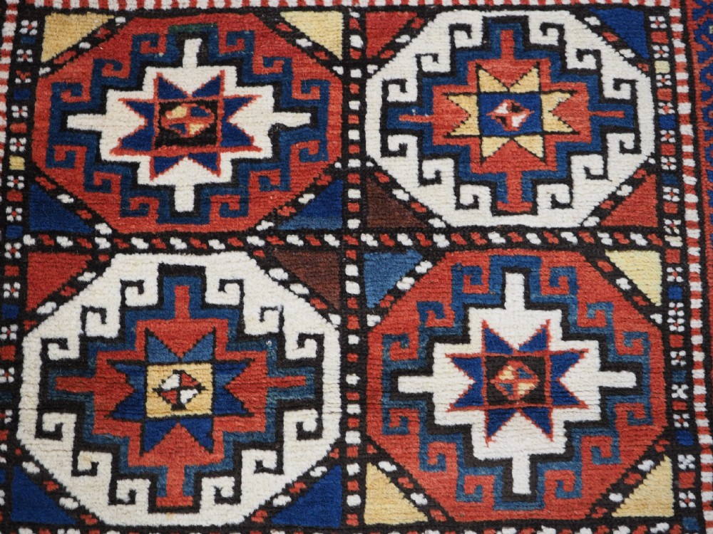An antique Caucasian Moghan Kazak long wool rug featuring two vertical columns of octagonal geometric medallions in red, navy blue, cream, yellow, and green within a decorative patterned border. View VIII