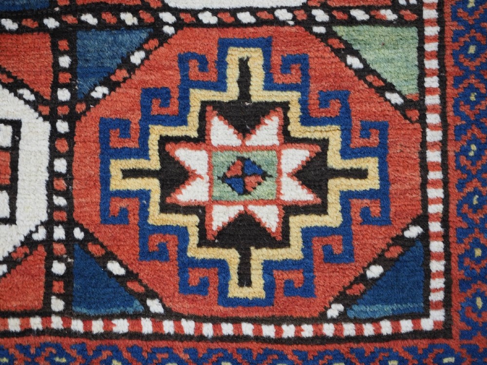 An antique Caucasian Moghan Kazak long wool rug featuring two vertical columns of octagonal geometric medallions in red, navy blue, cream, yellow, and green within a decorative patterned border. View XI