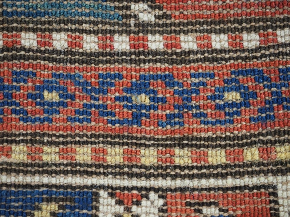 An antique Caucasian Moghan Kazak long wool rug featuring two vertical columns of octagonal geometric medallions in red, navy blue, cream, yellow, and green within a decorative patterned border. View XII
