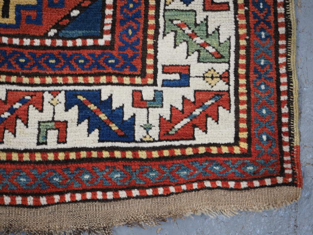 An antique Caucasian Moghan Kazak long wool rug featuring two vertical columns of octagonal geometric medallions in red, navy blue, cream, yellow, and green within a decorative patterned border. View XIII