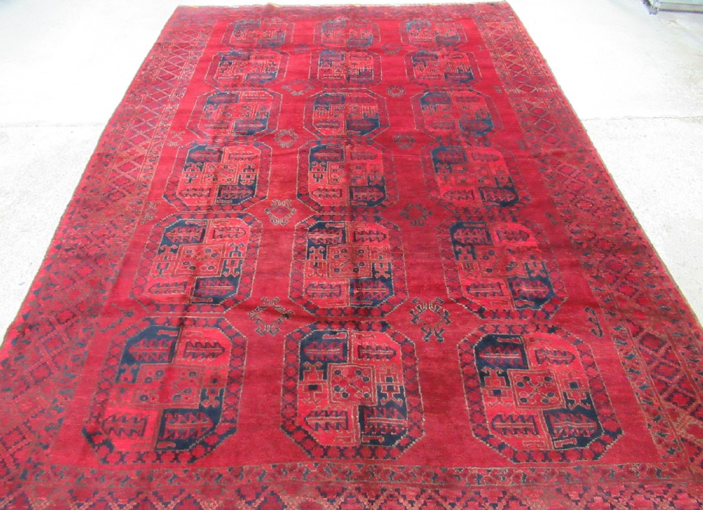 An antique red hand-knotted wool carpet featuring a repeating grid pattern of dark navy octagonal Ersari gul motifs and geometric borders.