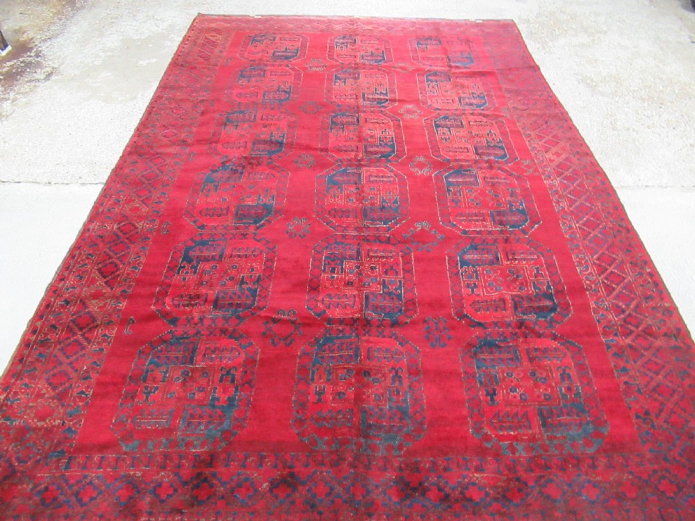 An antique red hand-knotted wool carpet featuring a repeating grid pattern of dark navy octagonal Ersari gul motifs and geometric borders. View II