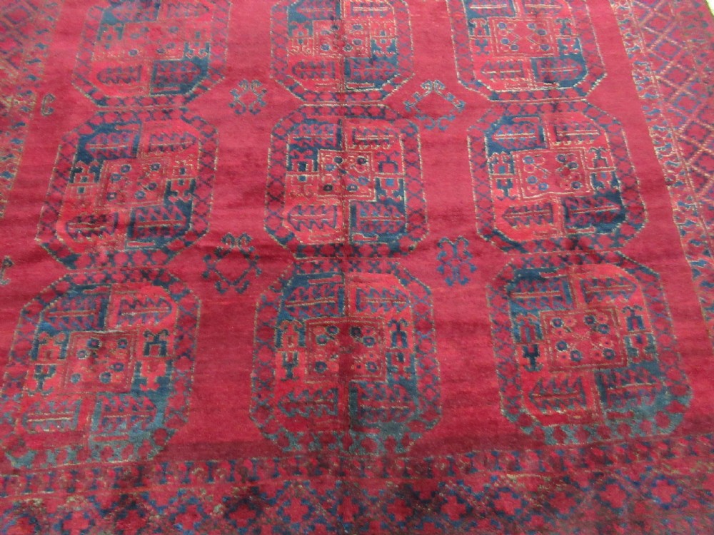 An antique red hand-knotted wool carpet featuring a repeating grid pattern of dark navy octagonal Ersari gul motifs and geometric borders. View III