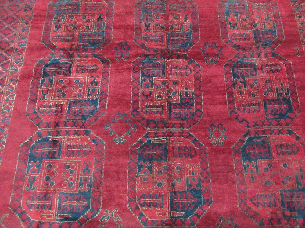 An antique red hand-knotted wool carpet featuring a repeating grid pattern of dark navy octagonal Ersari gul motifs and geometric borders. View IV
