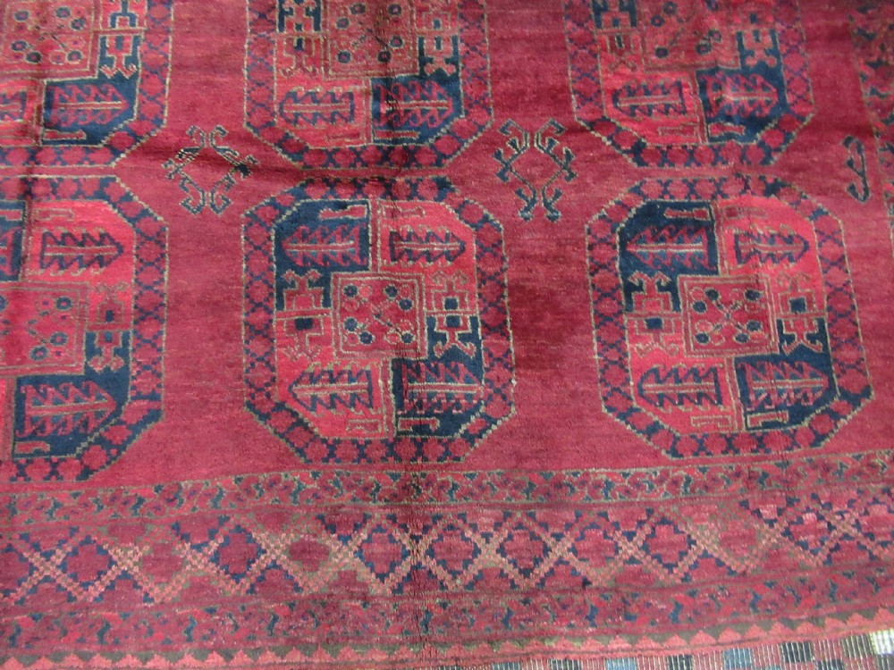 An antique red hand-knotted wool carpet featuring a repeating grid pattern of dark navy octagonal Ersari gul motifs and geometric borders. View V
