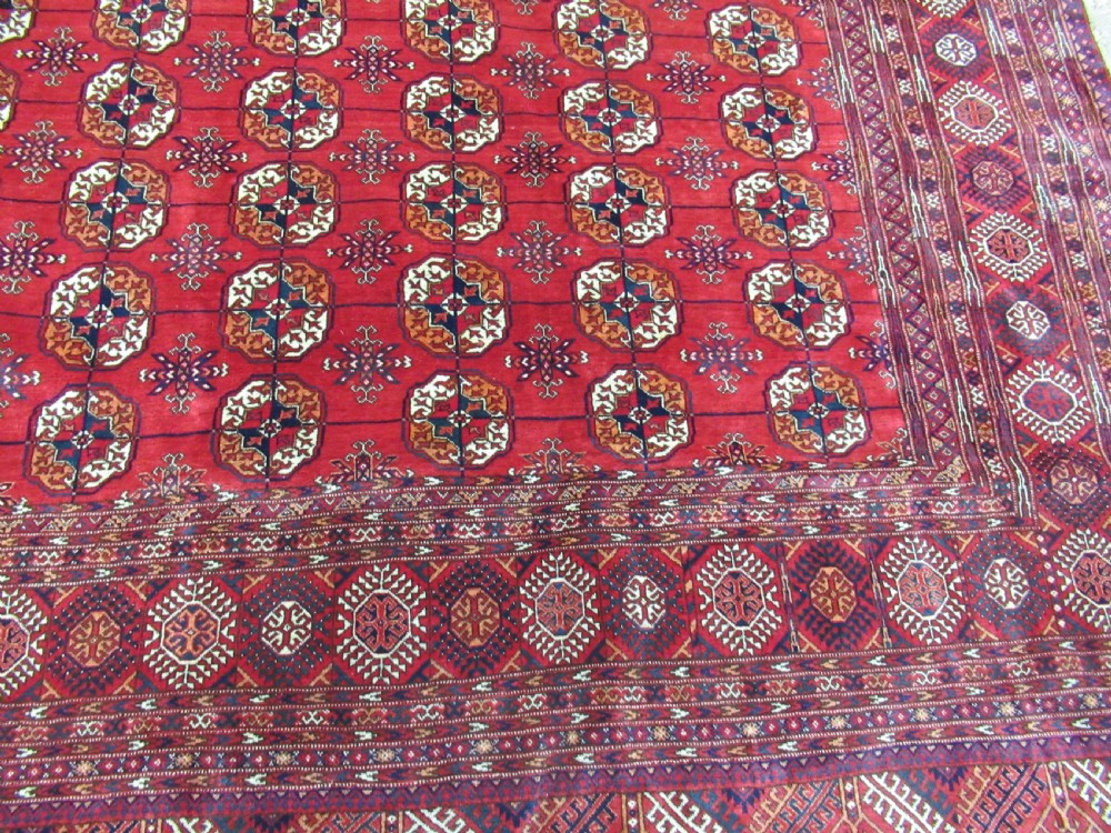 A large antique hand-knotted wool rug featuring repeating geometric gul motifs on a red field surrounded by multiple patterned borders. View II