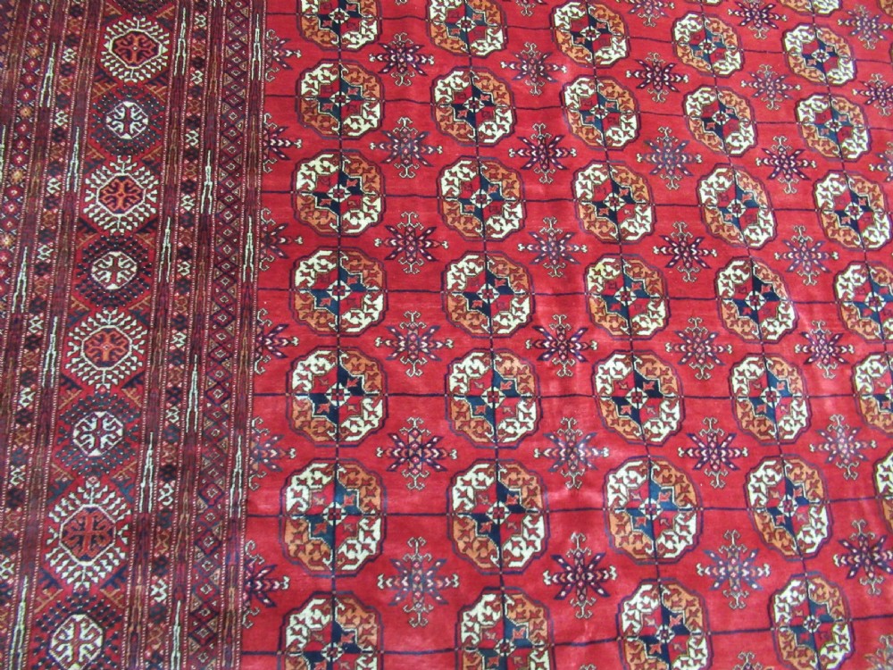 A large antique hand-knotted wool rug featuring repeating geometric gul motifs on a red field surrounded by multiple patterned borders. View III