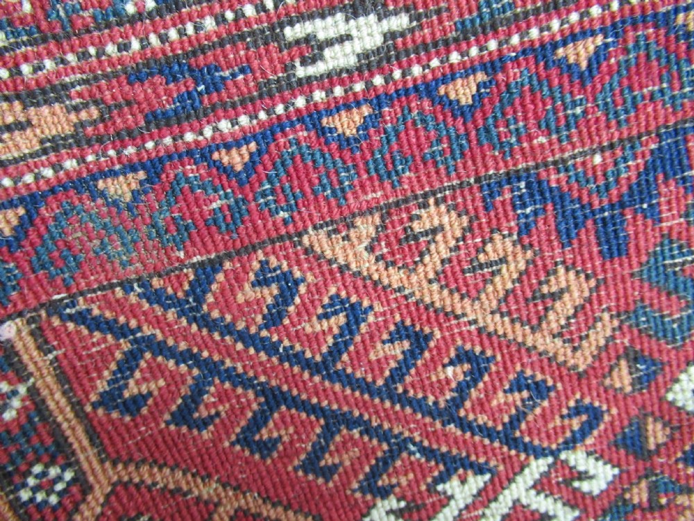 A large antique hand-knotted wool rug featuring repeating geometric gul motifs on a red field surrounded by multiple patterned borders. View IV