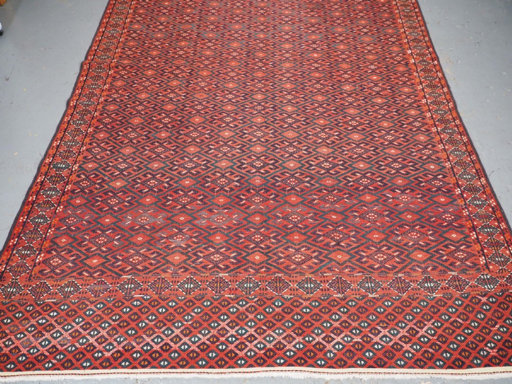 A large rectangular deep red wool flatweave carpet featuring an all-over diamond lattice pattern with detailed geometric borders and palas ends. View V