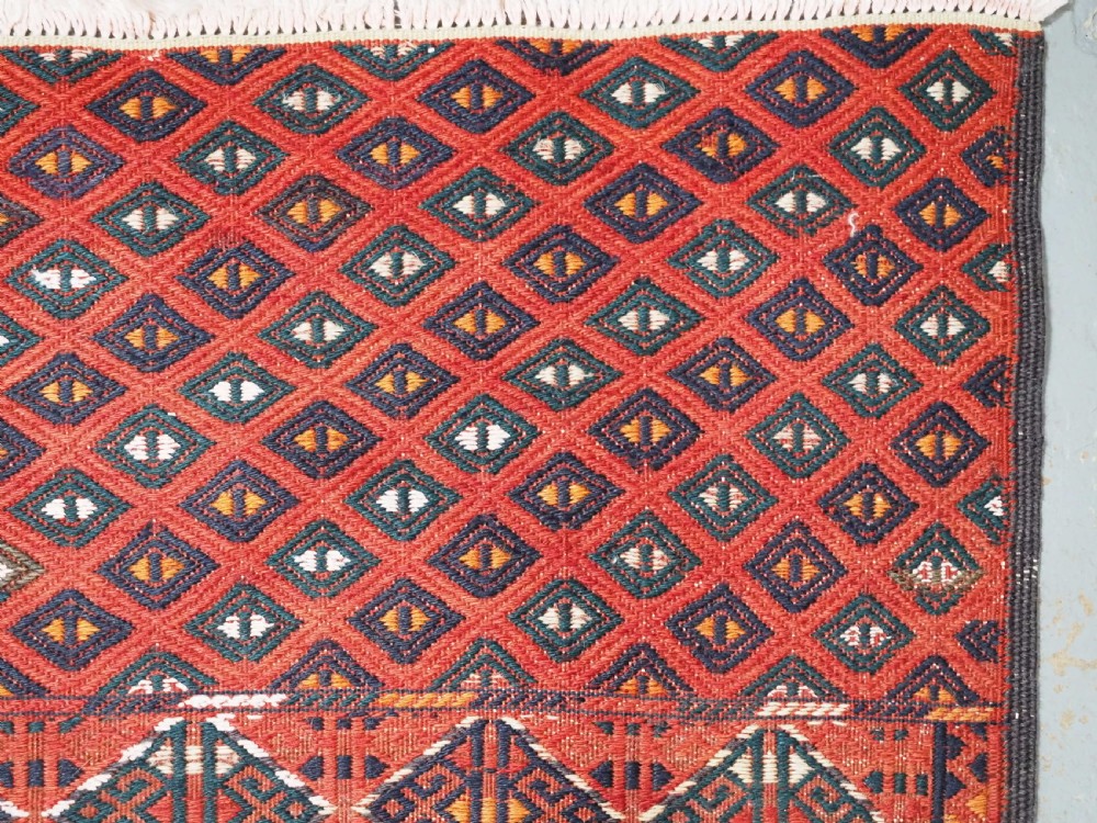 A large rectangular deep red wool flatweave carpet featuring an all-over diamond lattice pattern with detailed geometric borders and palas ends. View VI