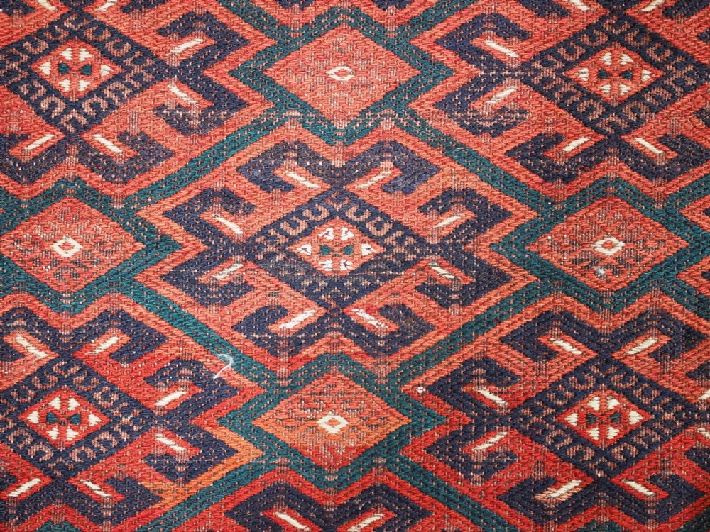 A large rectangular deep red wool flatweave carpet featuring an all-over diamond lattice pattern with detailed geometric borders and palas ends. View IX
