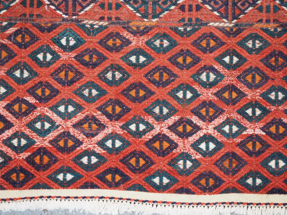 A large rectangular deep red wool flatweave carpet featuring an all-over diamond lattice pattern with detailed geometric borders and palas ends. View X