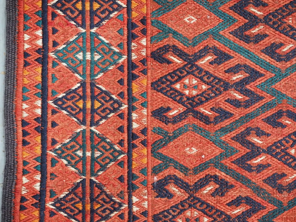 A large rectangular deep red wool flatweave carpet featuring an all-over diamond lattice pattern with detailed geometric borders and palas ends. View XII