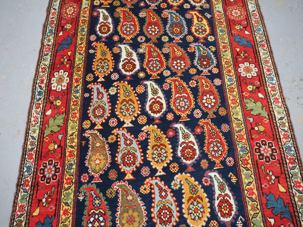 An antique Caucasian Karabagh hand-knotted wool runner rug featuring repeating multi-coloured boteh patterns on a dark navy field surrounded by a red floral border. View IV