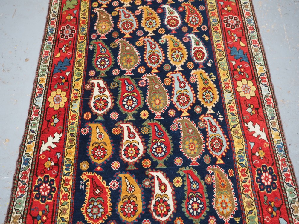 An antique Caucasian Karabagh hand-knotted wool runner rug featuring repeating multi-coloured boteh patterns on a dark navy field surrounded by a red floral border. View V