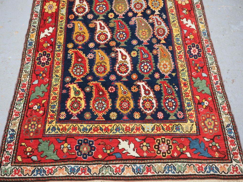 An antique Caucasian Karabagh hand-knotted wool runner rug featuring repeating multi-coloured boteh patterns on a dark navy field surrounded by a red floral border. View VI
