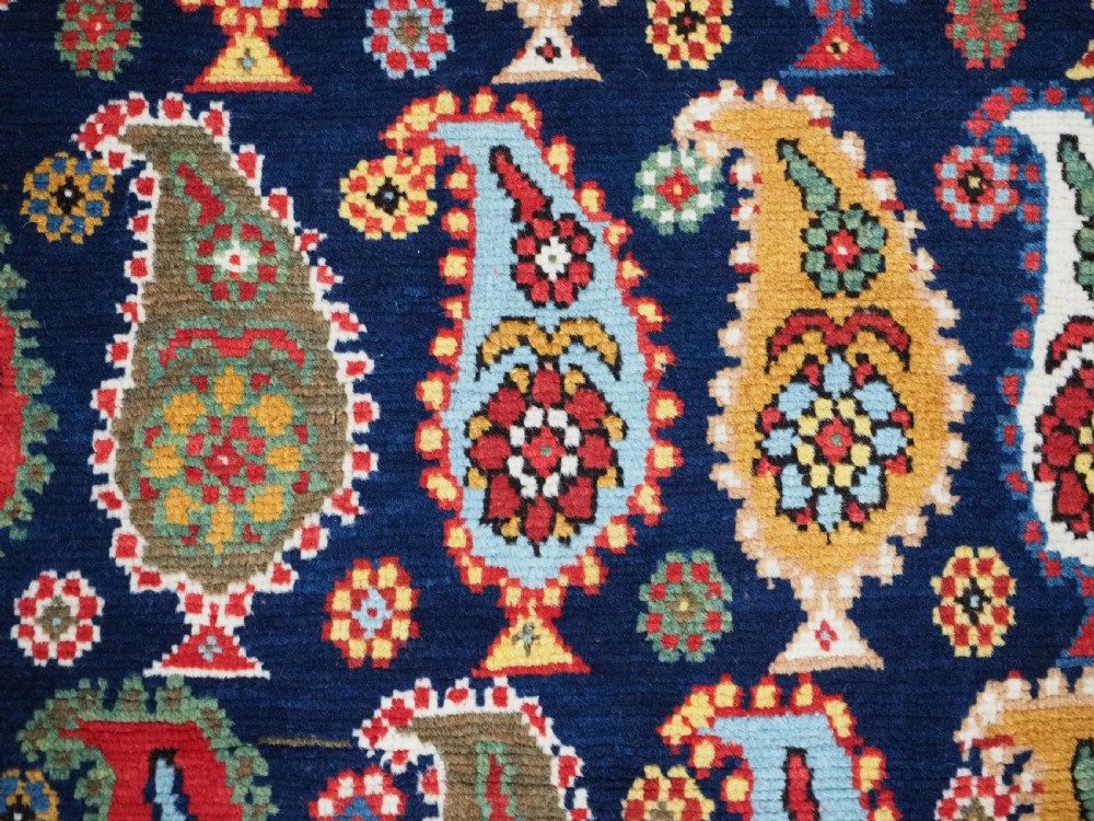An antique Caucasian Karabagh hand-knotted wool runner rug featuring repeating multi-coloured boteh patterns on a dark navy field surrounded by a red floral border. View X