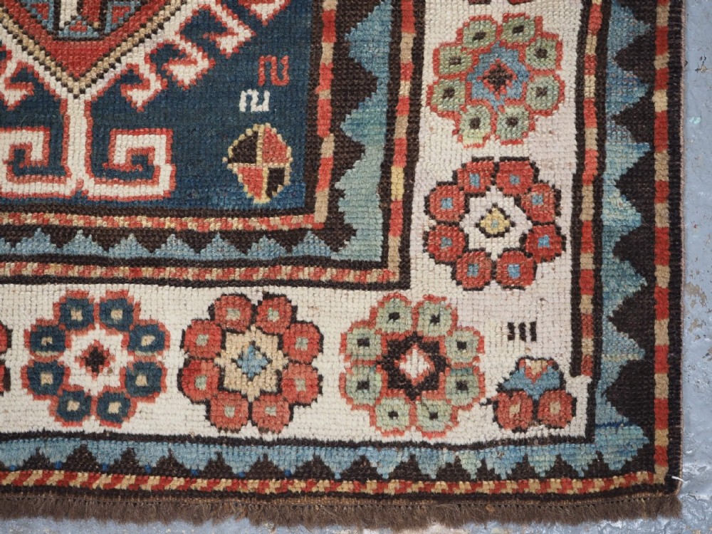An elongated hand-knotted wool carpet featuring two central red field columns filled with geometric latch hook medallions framed by a multi-tiered cream and blue geometric border. View XIII