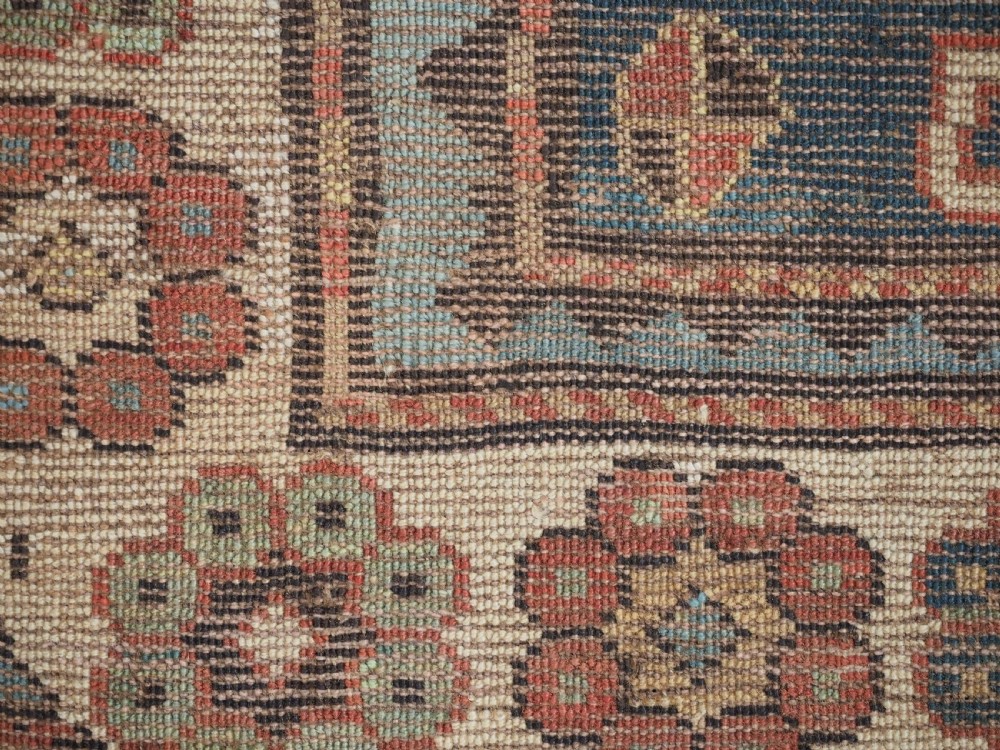 An elongated hand-knotted wool carpet featuring two central red field columns filled with geometric latch hook medallions framed by a multi-tiered cream and blue geometric border. View XIV