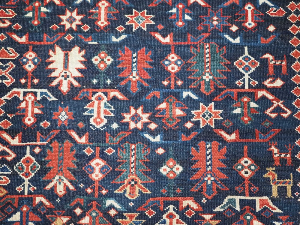 An antique hand-knotted wool rug featuring a dark navy central field filled with geometric tribal motifs, framed by multi-layered borders in red, cream, and blue hues. View VIII