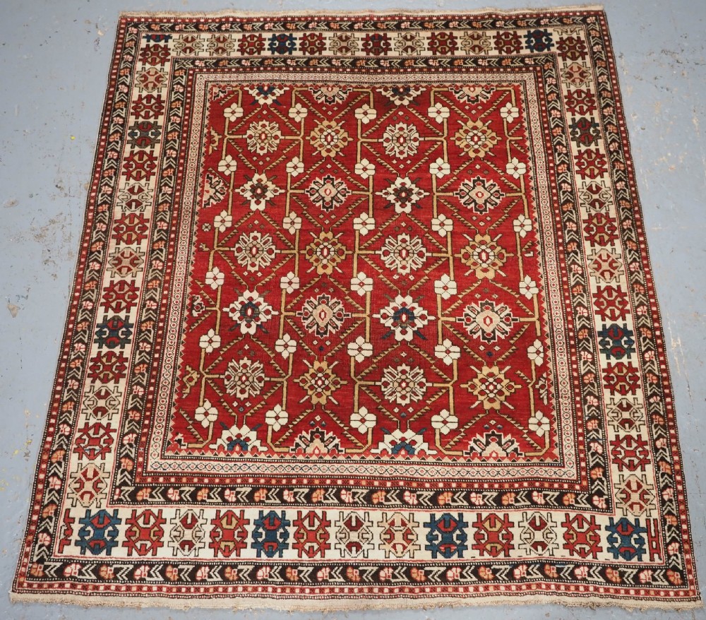 An antique hand-knotted Shirvan wool rug featuring a red field with an intricate cream floral lattice pattern framed by multi-layered geometric borders.