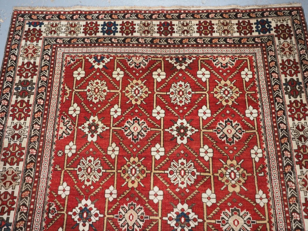 An antique hand-knotted Shirvan wool rug featuring a red field with an intricate cream floral lattice pattern framed by multi-layered geometric borders. View II