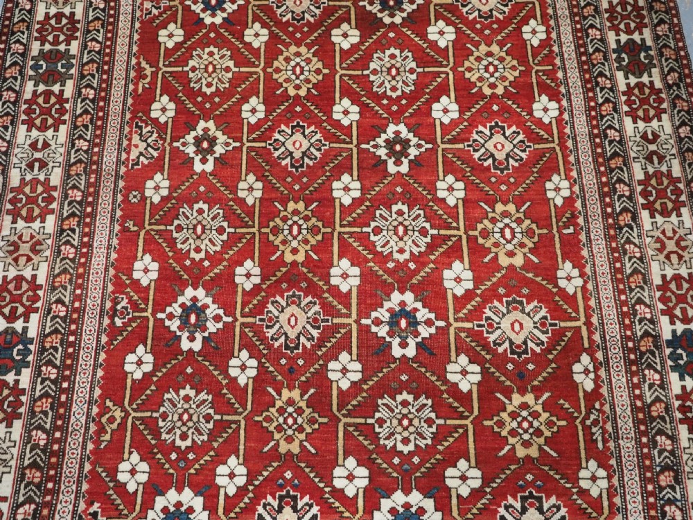An antique hand-knotted Shirvan wool rug featuring a red field with an intricate cream floral lattice pattern framed by multi-layered geometric borders. View III