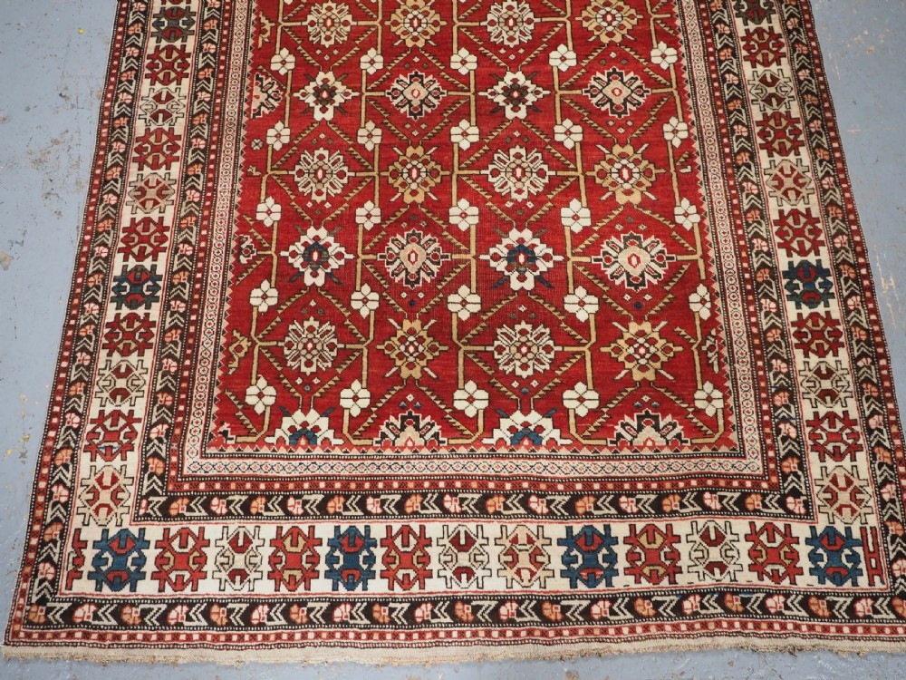 An antique hand-knotted Shirvan wool rug featuring a red field with an intricate cream floral lattice pattern framed by multi-layered geometric borders. View IV