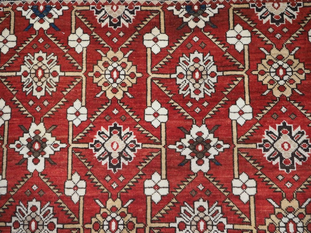 An antique hand-knotted Shirvan wool rug featuring a red field with an intricate cream floral lattice pattern framed by multi-layered geometric borders. View VII