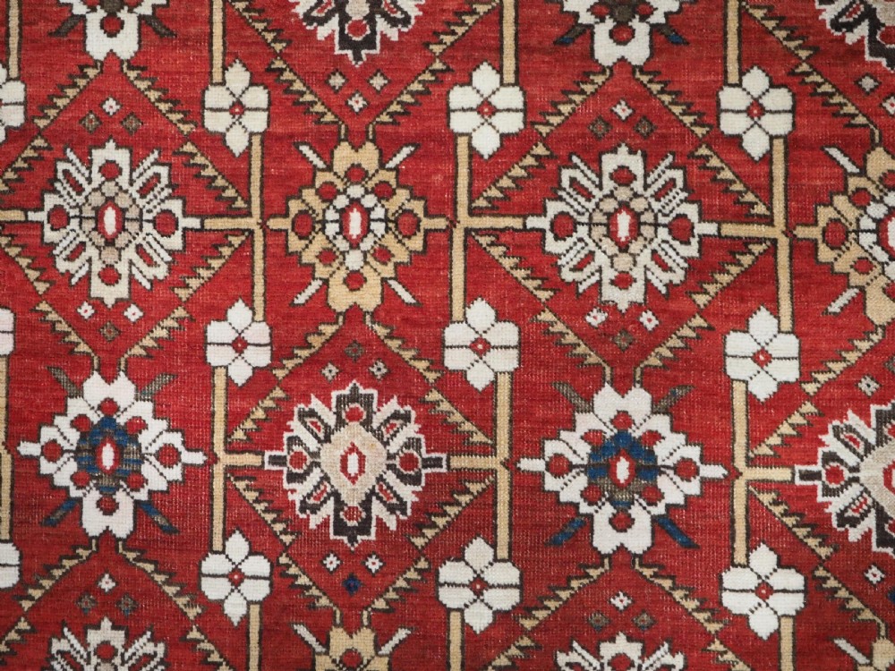 An antique hand-knotted Shirvan wool rug featuring a red field with an intricate cream floral lattice pattern framed by multi-layered geometric borders. View VIII