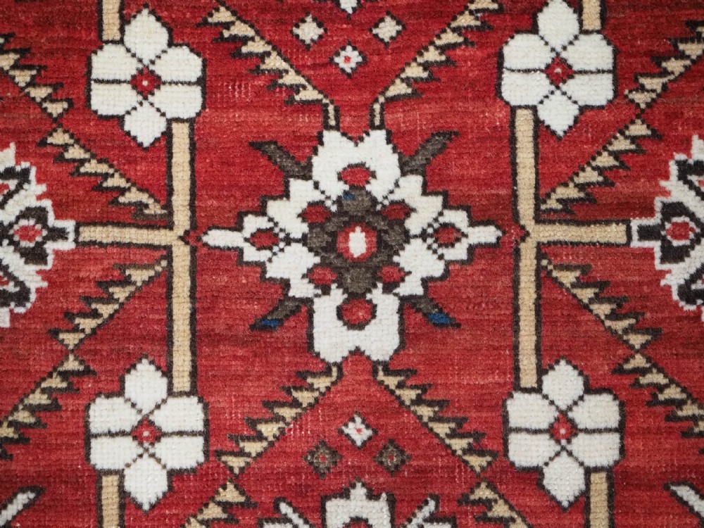 An antique hand-knotted Shirvan wool rug featuring a red field with an intricate cream floral lattice pattern framed by multi-layered geometric borders. View XI