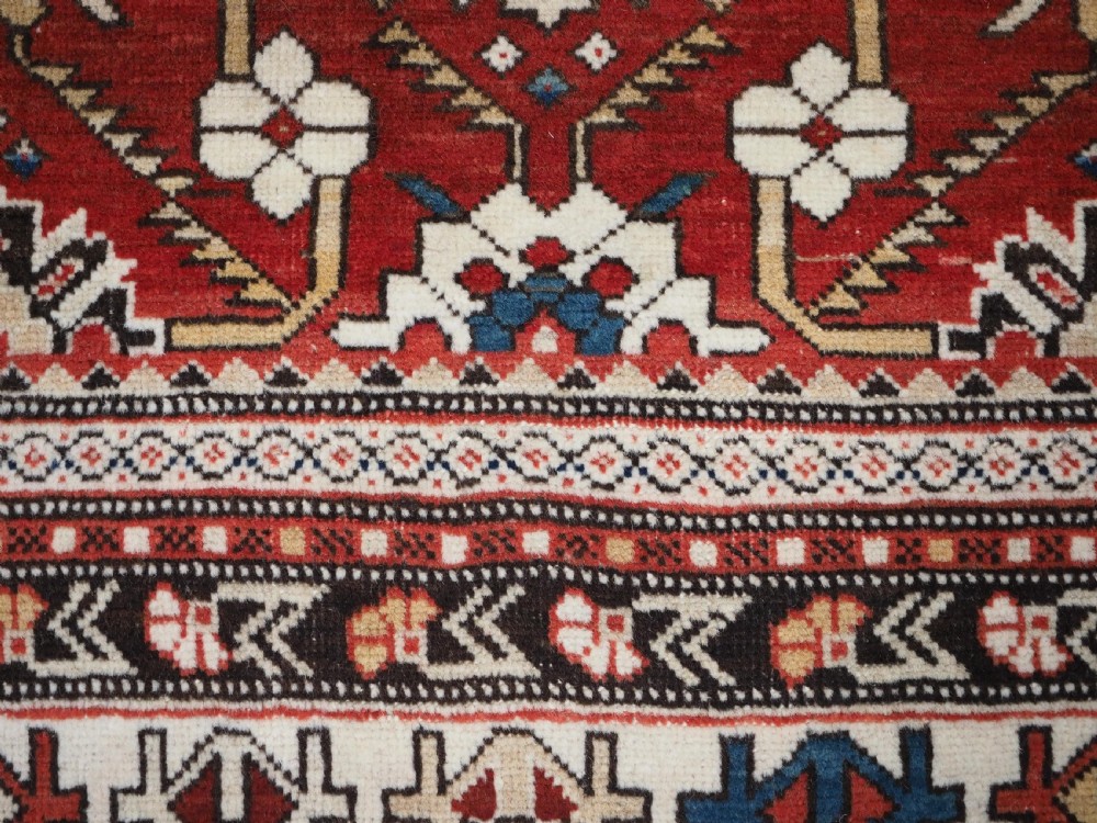 An antique hand-knotted Shirvan wool rug featuring a red field with an intricate cream floral lattice pattern framed by multi-layered geometric borders. View XII