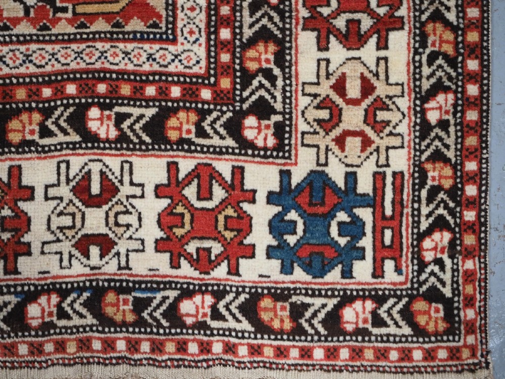 An antique hand-knotted Shirvan wool rug featuring a red field with an intricate cream floral lattice pattern framed by multi-layered geometric borders. View XIII