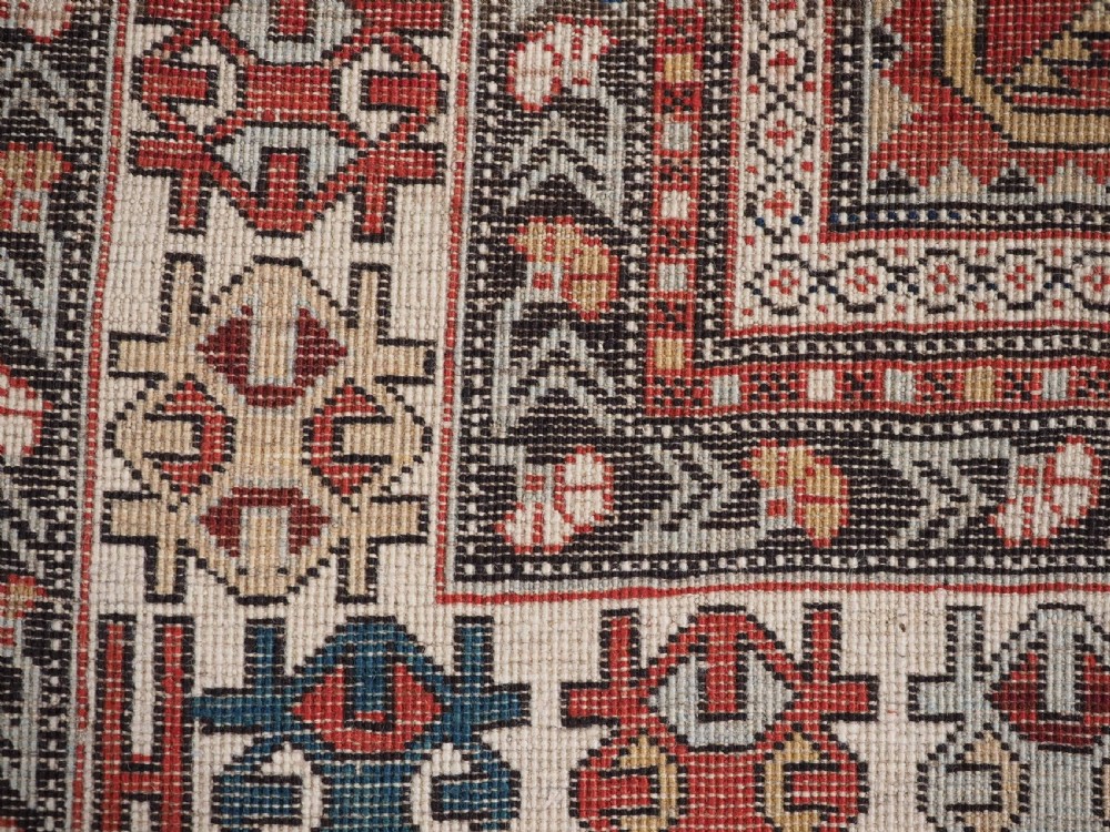 An antique hand-knotted Shirvan wool rug featuring a red field with an intricate cream floral lattice pattern framed by multi-layered geometric borders. View XIV