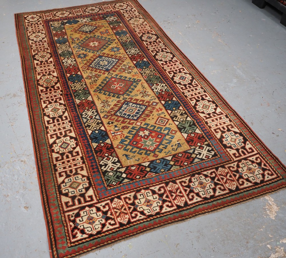 An antique South Caucasian hand-knotted wool rug with a vibrant yellow central field, diamond medallions, and ornate multi-coloured geometric borders. View II