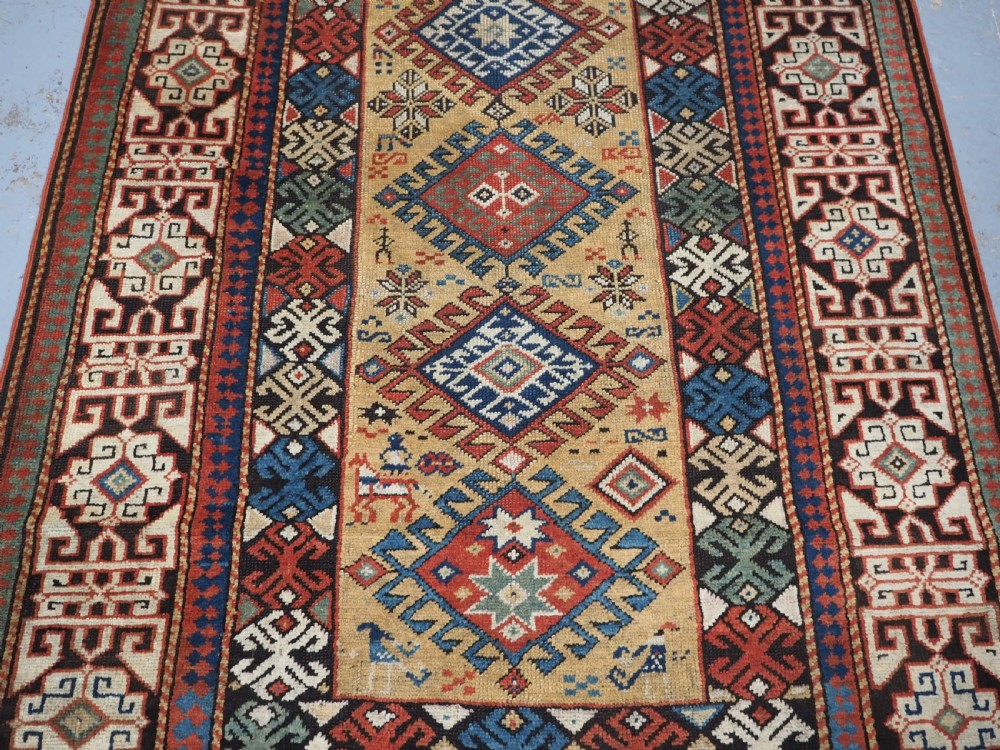 An antique South Caucasian hand-knotted wool rug with a vibrant yellow central field, diamond medallions, and ornate multi-coloured geometric borders. View V