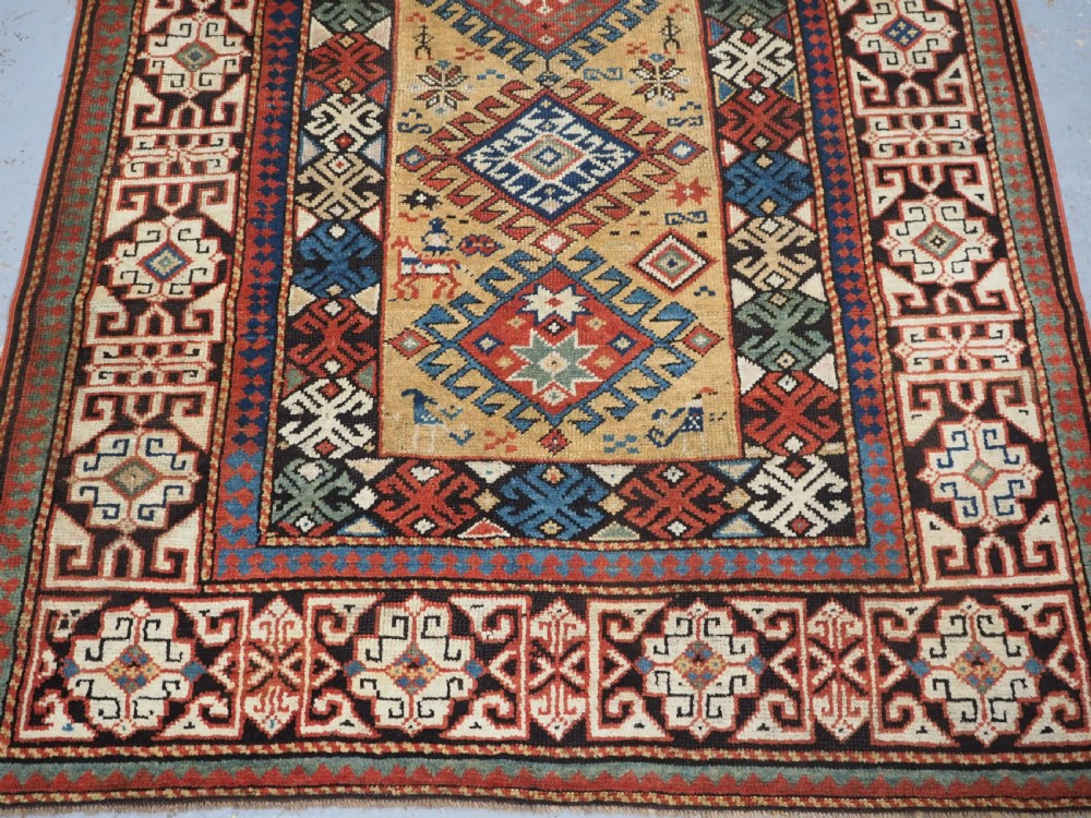 An antique South Caucasian hand-knotted wool rug with a vibrant yellow central field, diamond medallions, and ornate multi-coloured geometric borders. View VI