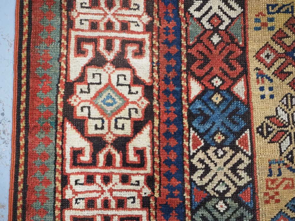 An antique South Caucasian hand-knotted wool rug with a vibrant yellow central field, diamond medallions, and ornate multi-coloured geometric borders. View VIII
