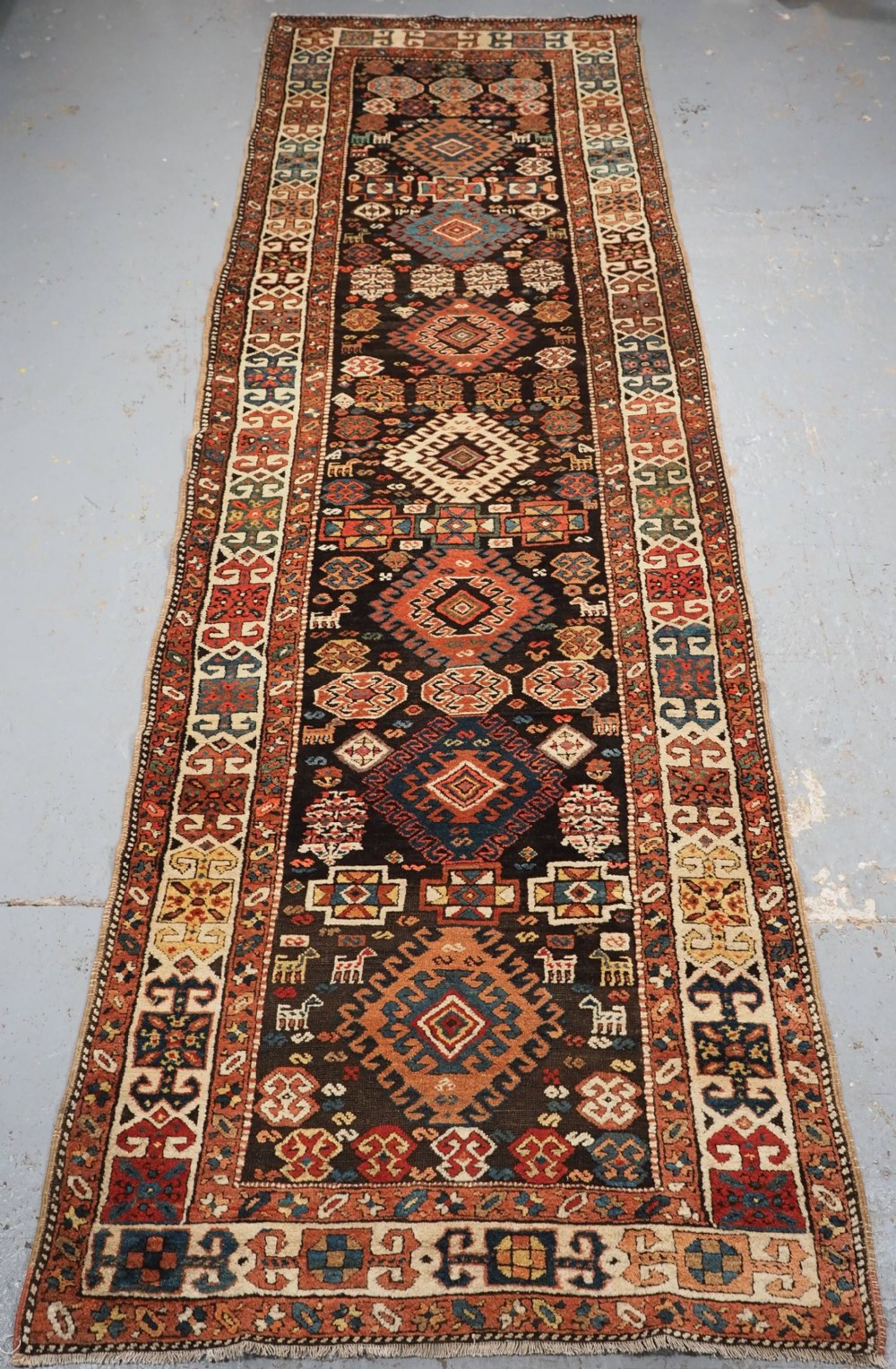 An antique Kurdish wool runner rug featuring a dark central field filled with diamond latch hook medallions and geometric polychrome borders.