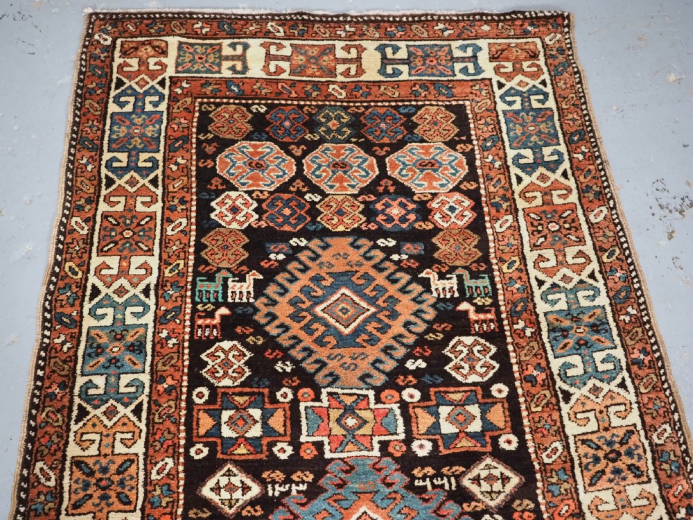 An antique Kurdish wool runner rug featuring a dark central field filled with diamond latch hook medallions and geometric polychrome borders. View II