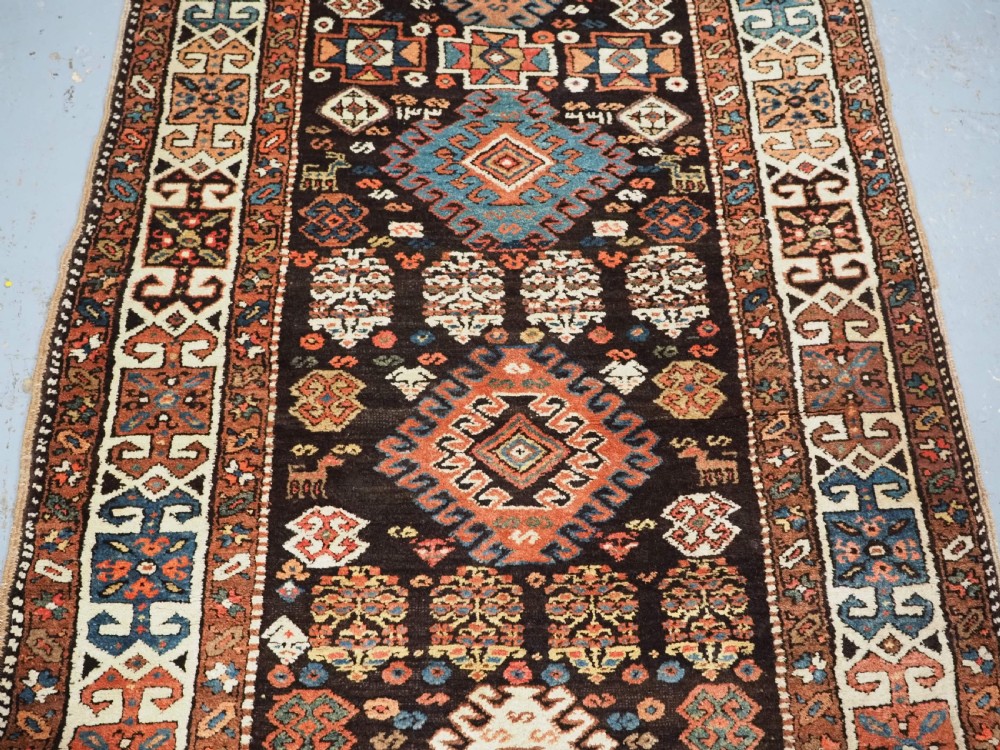 An antique Kurdish wool runner rug featuring a dark central field filled with diamond latch hook medallions and geometric polychrome borders. View III