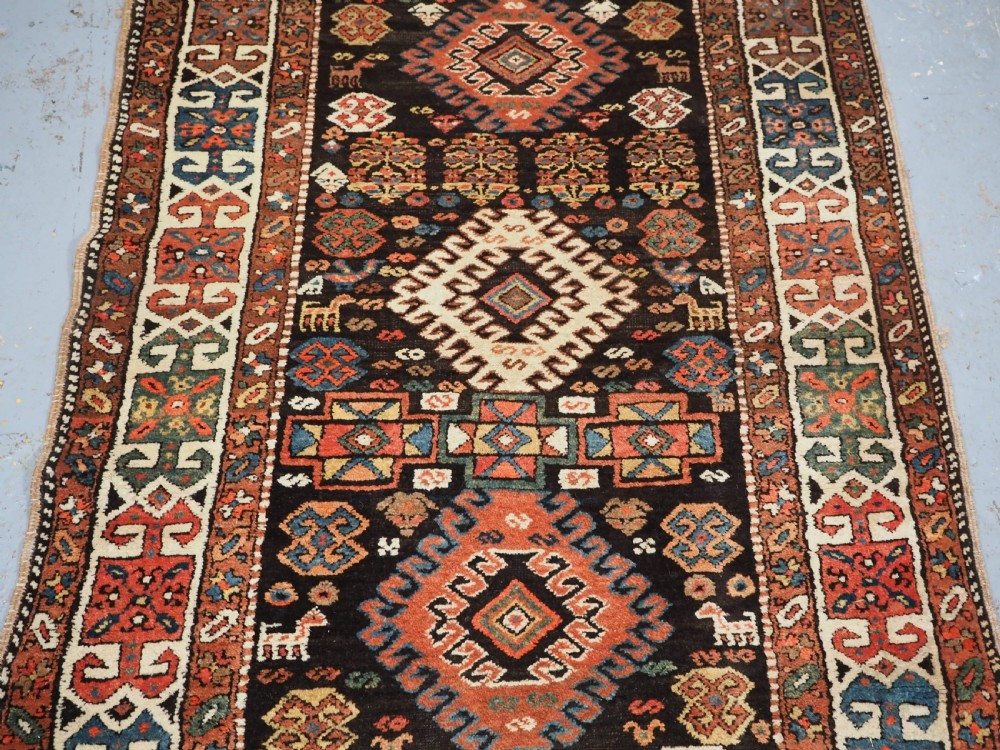 An antique Kurdish wool runner rug featuring a dark central field filled with diamond latch hook medallions and geometric polychrome borders. View IV