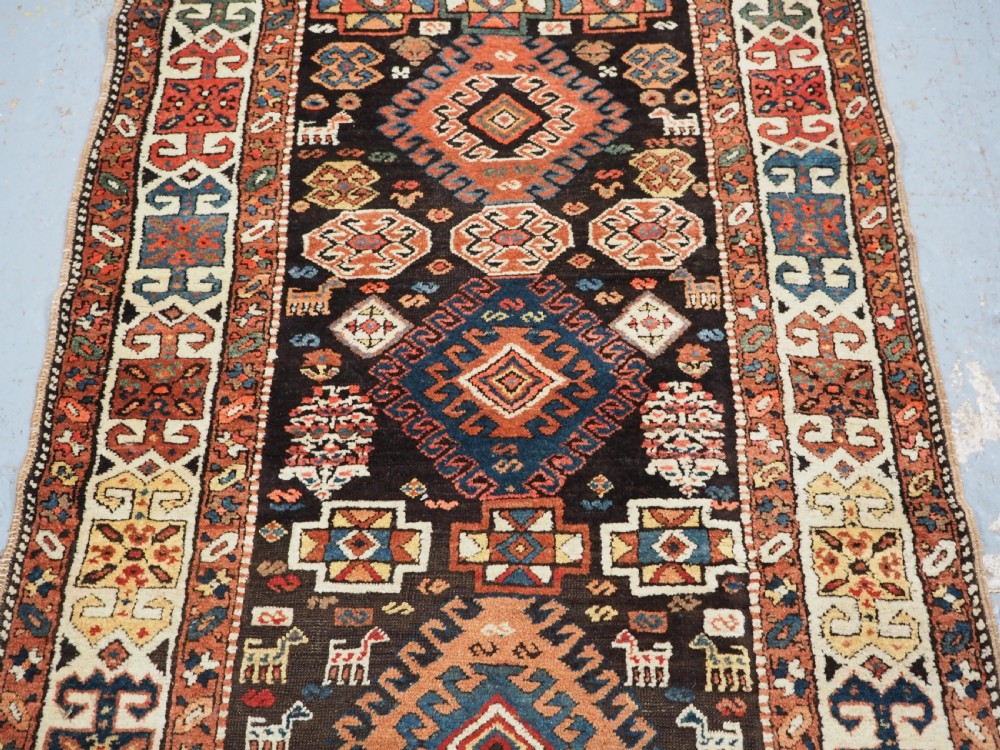 An antique Kurdish wool runner rug featuring a dark central field filled with diamond latch hook medallions and geometric polychrome borders. View V