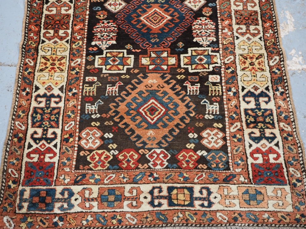 An antique Kurdish wool runner rug featuring a dark central field filled with diamond latch hook medallions and geometric polychrome borders. View VI