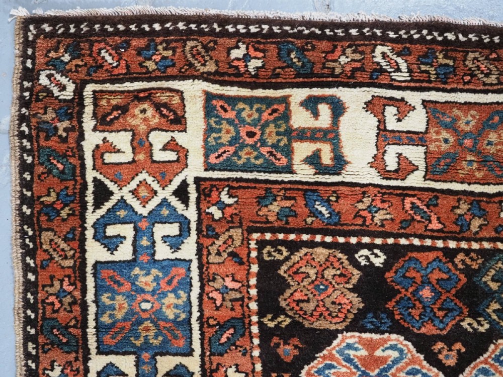 An antique Kurdish wool runner rug featuring a dark central field filled with diamond latch hook medallions and geometric polychrome borders. View VII