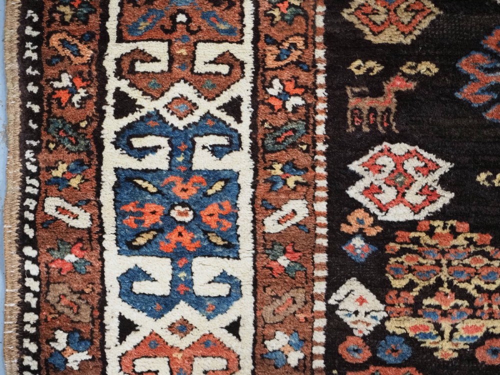 An antique Kurdish wool runner rug featuring a dark central field filled with diamond latch hook medallions and geometric polychrome borders. View VIII