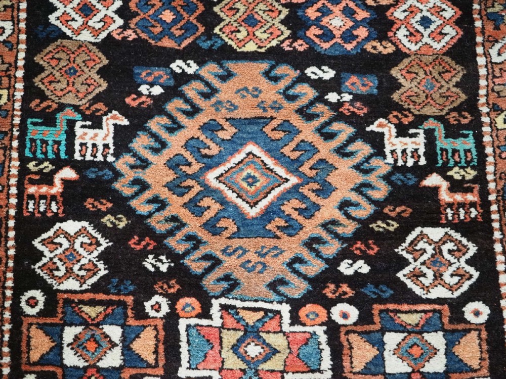 An antique Kurdish wool runner rug featuring a dark central field filled with diamond latch hook medallions and geometric polychrome borders. View IX