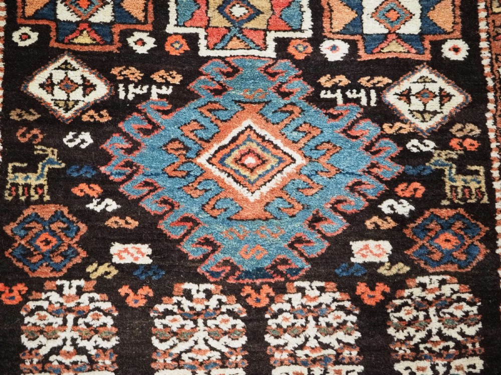 An antique Kurdish wool runner rug featuring a dark central field filled with diamond latch hook medallions and geometric polychrome borders. View X